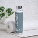 Personalisierte Bridesmaid Dusty Blue White Script Trinkflasche<br><div class="desc">Überraschen Sie Ihre Hochzeitsgal mit dieser Personalisierten Bridesmaid Dusty Blue White Script Water Flasche. Es ist modern und minimalistisch gestaltet und bietet einen individuell einstellbaren blauen Hintergrund. Der Text ist "überhängend" in großen weißen Schriftzeichen vertikal auf verlassen Vorderseite. Der Name ist in passendem handgeschriebenem Skript auf dem rechten unteren Bereich....</div>
