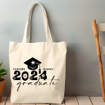 Personalisierte Graduate Class 2024 Tragetasche<br><div class="desc">Graduate Class of 2024 Quote verfügt über eine Kappe mit Tassel,  moderne Topographie und Kalligraphie-Skript,  mit Flora und Herzen Akzent. Einfach mit Ihrem Wunschnamen und dem Monogramm auf der Rückseite personalisieren. Eine tolle Geschenkidee für diesen besonderen Grad. (Schulfarbe: (schwarz)</div>