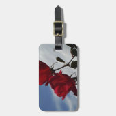 Rote Rosen gegen einen hellen blauen Himmel Gepäckanhänger (Vorderseite vertikal)