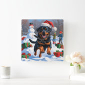 Rottweiler läuft im Schnee mit Weihnachtshut Quadratische Wanduhr (Zuhause)