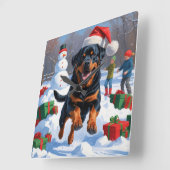 Rottweiler läuft im Schnee mit Weihnachtshut Quadratische Wanduhr (Winkel)