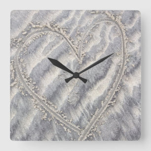 Schrulliges Herz, das im Sandquadrat zeichnet Quadratische Wanduhr