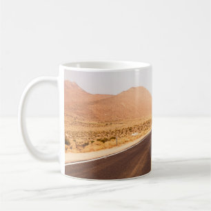 SCHWARZE ASPHALTSTRASSE INMITTEN DES BROWN-FELDES KAFFEETASSE