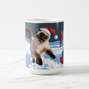 Siamische Katze läuft im Schnee mit Weihnachtsmütz Kaffeetasse