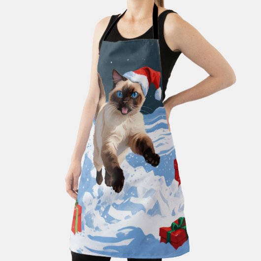 Siamische Katze läuft im Schnee mit Weihnachtsmütz Schürze (InSitu)