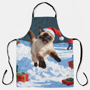 Siamkatze läuft im Schnee mit Weihnachtsmütze Schürze