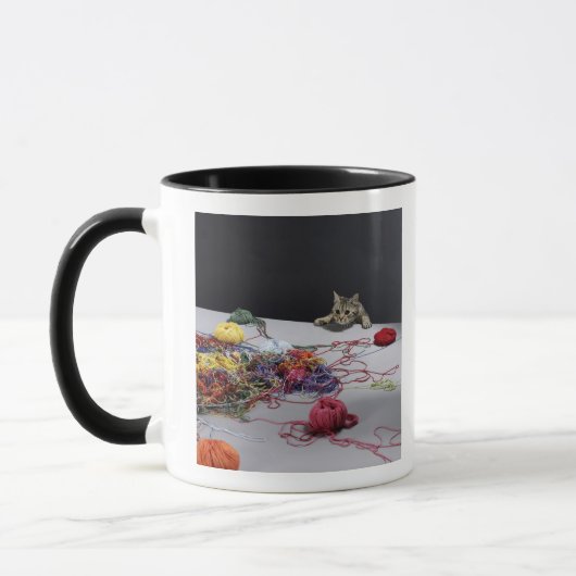 Silberne Tabbykatze, die über Rand der Tabelle Tasse (Links)