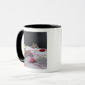 Silberne Tabbykatze, die über Rand der Tabelle Tasse (Vorderseite Links)