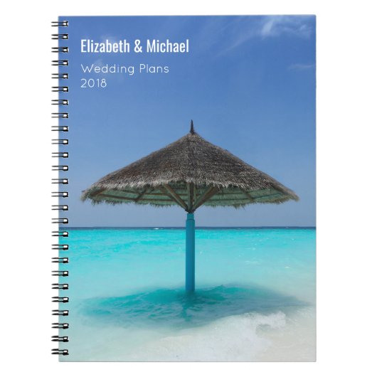 Sonnenschirm aus Strohdach auf Hochzeitsplänen von Notizblock (Vorderseite)