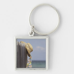 Strohhut, der am Zaun am Strand hängt Schlüsselanhänger