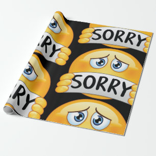 Trauriges Sorry Emoji Gesicht hält Entschuldigungs Geschenkpapier