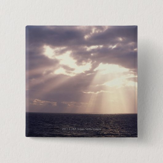 Untergehende Sonne, die durch Wolken über Ozean Button (Vorderseite)