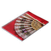 Verzierter Handheld-Lüfter auf einem roten Hinterg Notizblock (Linke Seite)