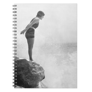 Weibliche Schwimmerin auf Felsen über tosenden Wel Notizblock