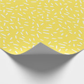Weiße Confetti-Sprinklen auf hellgelben Geschenkpapier (Ecke)