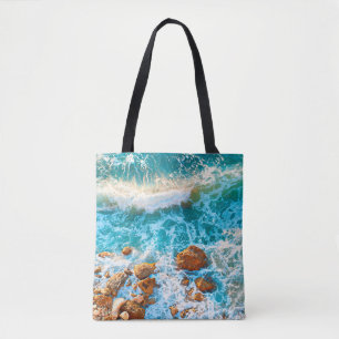 Wellen auf einem felsigen Strand bei Sonnenunterga Tasche